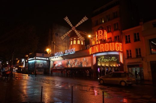 Moulin Rouge se zářícími červenými lopatkami za deštivého večera na Pigalle